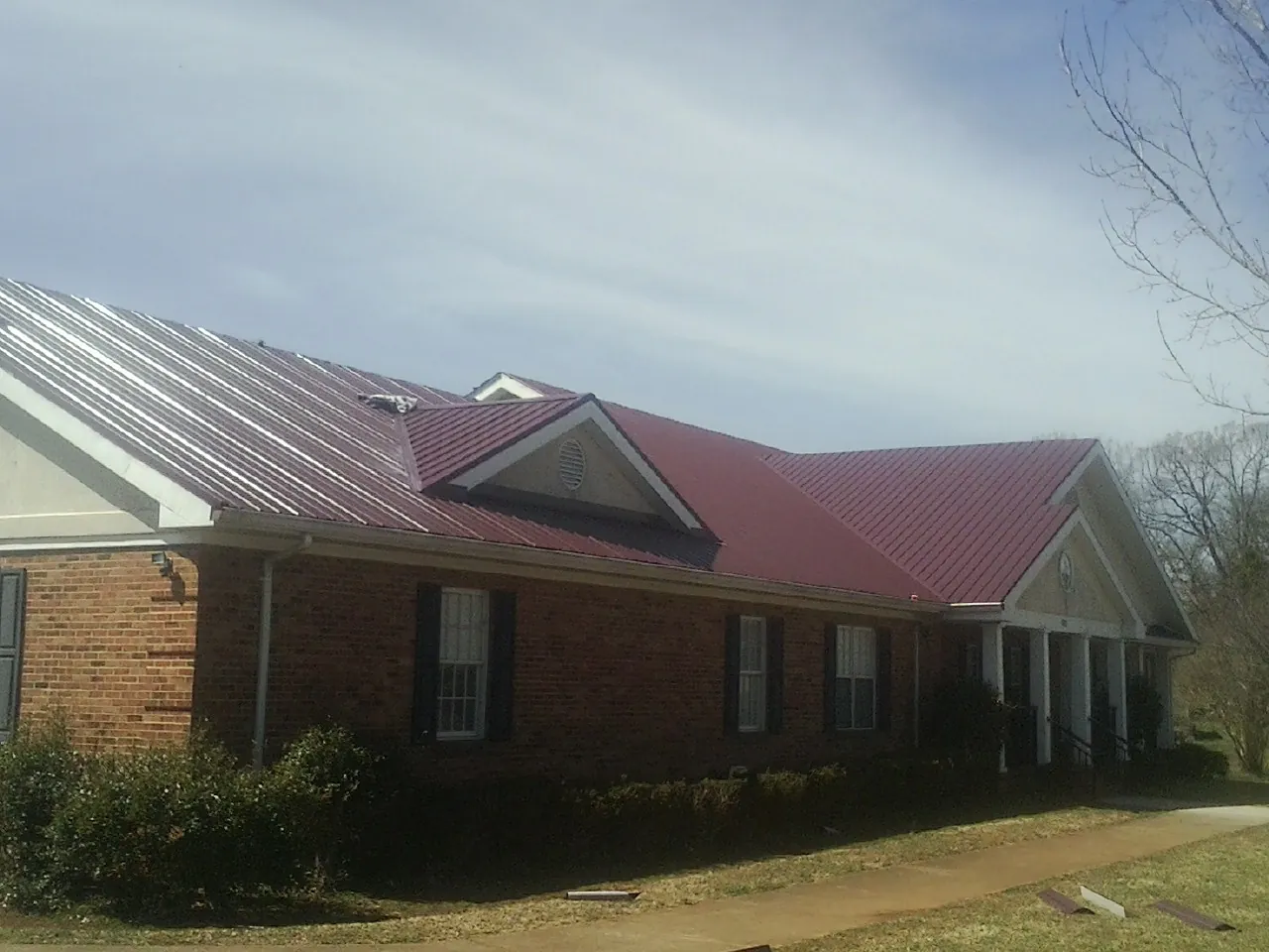 Red metal roof with gabled entries on a long brick building, from a Hail Damage Roof Repair job in Pinehurst