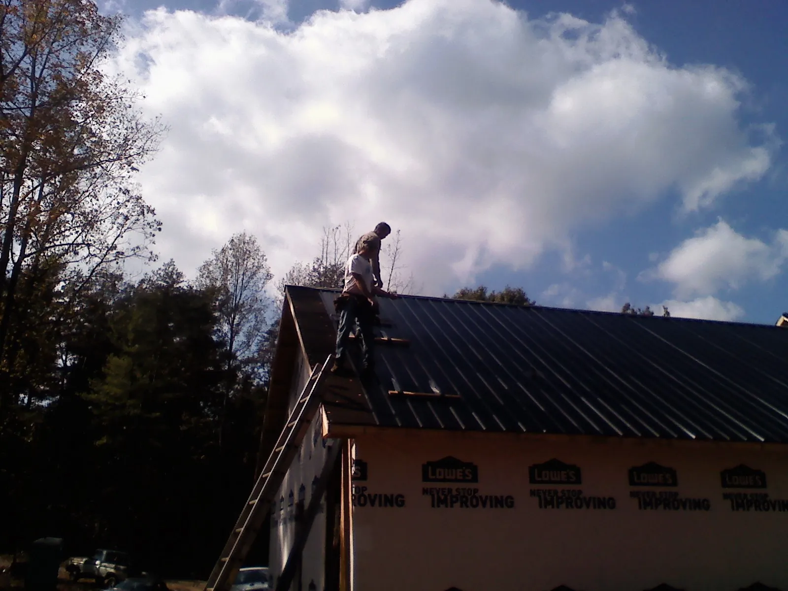 Roofer fastening dark metal panels high against a cloudy sky, from a Roof Inspection job in Pinehurst